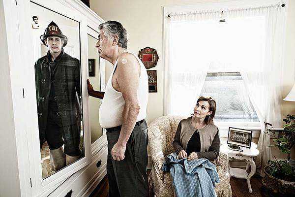 photograph of older man with wife looking in mirror and seeing reflection of his younger self as a fireman