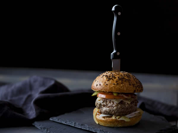 burger skewered with knife near black textile food photography inspiration